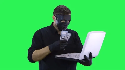 A masked computer hacker is talking via video link and showing the money earned. Video stock 132803598