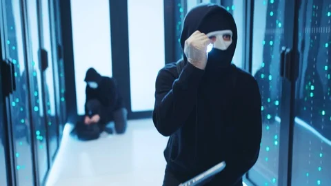 Masked computer hacker using flashlight checking server room, coding in malware Stock Footage 120694217