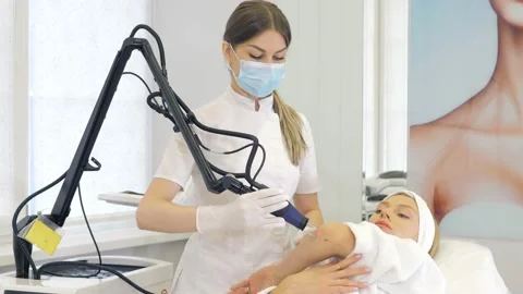 A masked cosmetologist-dermatologist performs hardware laser hair removal for a Video stock 169517149