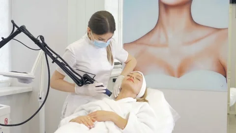 A masked cosmetologist performs hardware laser hair removal for a beautiful girl Stock Footage 169518408