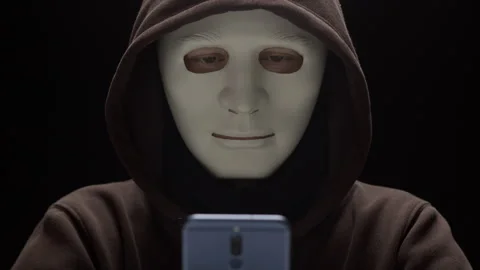 Masked criminal uses phone to commit fraud. Concept of hacking and cybersecurity Stock Footage 303913062