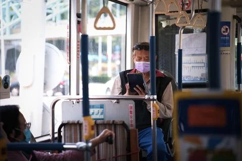 Masked elderly man using tablet alone on Taipei city bus during pandemic Stock-Fotos