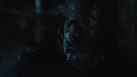 Masked figure lowering head into shadow with slow tilt, rim lit mask edges, dark 库存影片 343684531