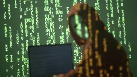 Masked Hacker in Hoodie Looking Back While Coding on Laptop with Green Stock Footage 307177191