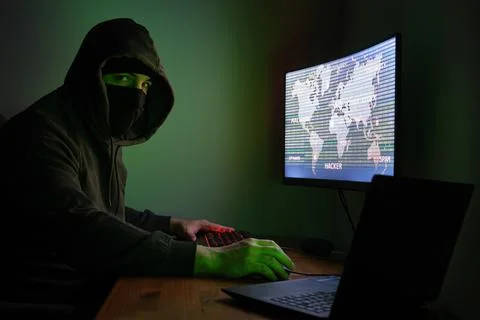 Masked hacker looking at camera is using a computer for organizing data attack 스톡 사진