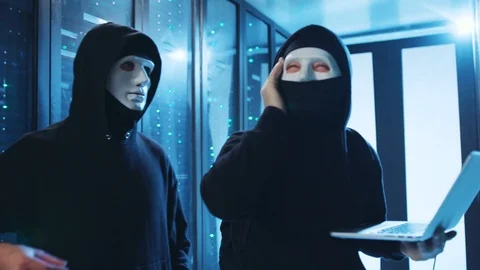 Masked hacker suffering headache when coding in server room. His partner 스톡 동영상 120694908