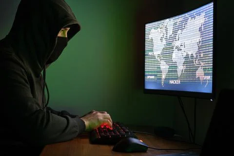 Masked hacker typing in a computer for organizing massive data breach attack Stock Photos