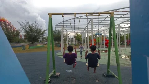 Masked kids playing on a swing in a public park Stock Footage