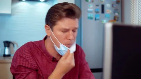 Masked man coughs at home while working at the computer Stock Footage 144986486