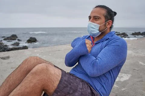 Masked man performs sit-ups in front of the sea. New normality. Sports Stock Photos