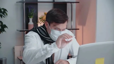 A masked man sitting at a table in front of a laptop indicates . Stock Footage 147668730