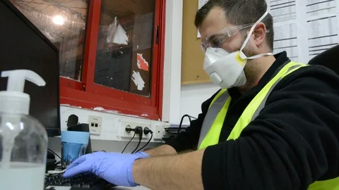 A masked man at a table works on a computer in office. Stock Footage 127191841