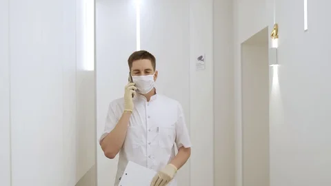 A masked man walks down the corridor at a modern clinic and talks on the phone Stock Footage 130019366