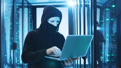 Masked network hacker using laptop to break a server in digital room. Scared Stock Footage 120695116