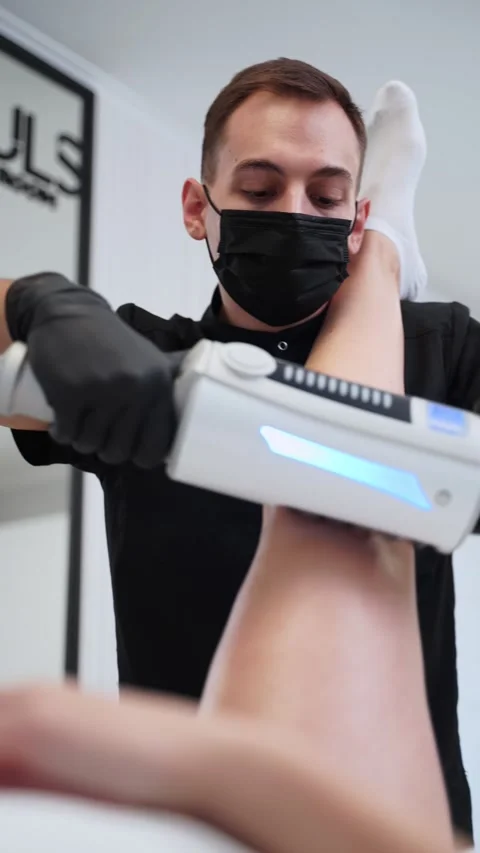 Masked professional performs endospheres therapy on clients leg at modern clinic Stock Footage 256910923