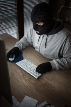 Masked thief sitting in front of computer Foto stock