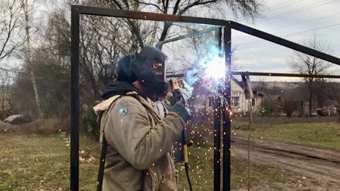 A masked welder is welding the iron structure of the gate Stock Footage 229494964