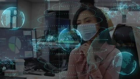 Masked woman reviewing data while monitor updating, AR globes growing, marking Stockbeeldmateriaal 331005782