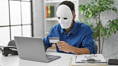 Masked young latin man pulls off a daring credit card hack on his laptop at.. Video stock 262757294