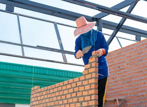 Mason bricklayer installing red clay bricks on a wall at a construction site. Stock Photos