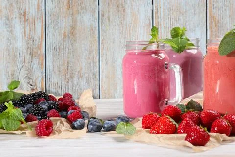 Mason jars of different berry smoothies and fresh ingredients on white wood.. Stock Photos
