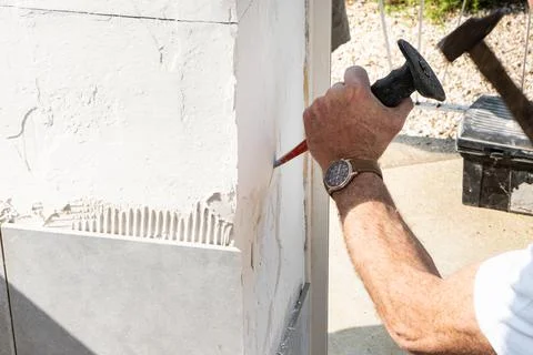 The mason prepares the wall with a chisel before laying a ceramic tile Stock Photos