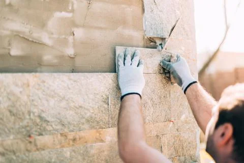 Mason worker installing stone tiles on wall on construction site Stock Photos