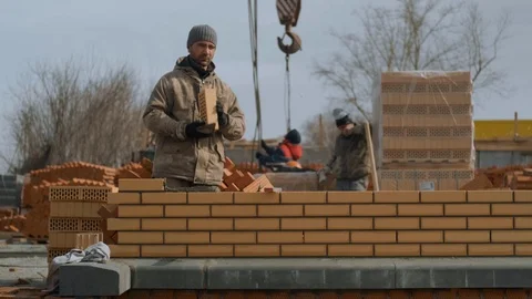 Mason Worker Puts Brickwork, Young Smiling Bricklayer Builds Brick Building Stock Footage 129499433