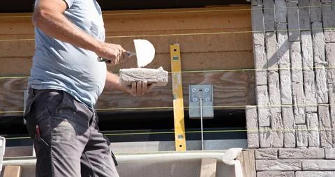 Masonry worker the bricklayer makes the facade of the house from gray bricks Stock Photos