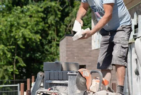 Masonry worker the bricklayer makes the facade of the house from gray bricks Stock Photos
