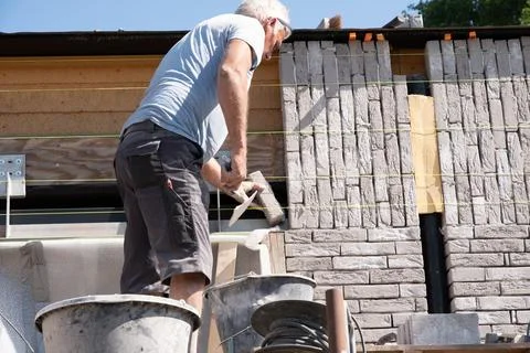Masonry worker the bricklayer makes the facade of the house from gray bricks Stock Photos