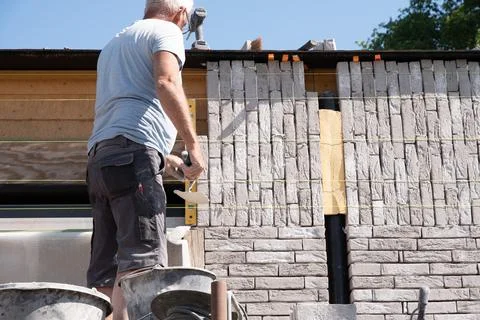 Masonry worker the bricklayer makes the facade of the house from gray bricks Stock Photos