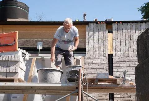 Masonry worker the bricklayer makes the facade of the house from gray bricks Stock Photos