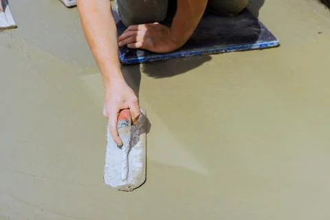 Masonry worker works on construction site, spreading cement on floor using tr Stock Photos