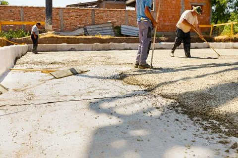 Masons, workers are using rake to level fresh concrete over reinforcing ste.. Stock Photos