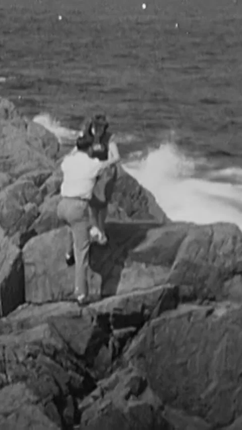 MASSACHUSETTS - 1947 - Two lovers meet on a rocky shore as the waves crash Stock Footage 338427016