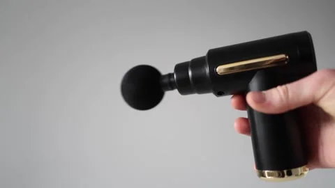 Massage gun in action, held in a hand against a neutral background. The device v Stock Footage 303908383