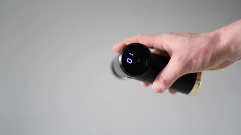 Massage gun with digital display held in hand against neutral background, demons Stock Footage 303908378
