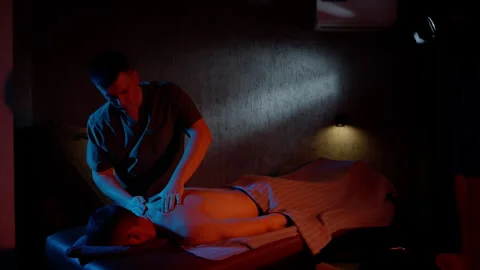 Massage room, self care, man massages man's back in blue and red colors. As the Stock Footage 256582853