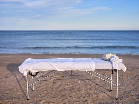 A massage table placed on the sand of a beach with the sea in the background. Stock Photos