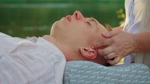 Massaging man temple for relaxation by river. Professional giving calming Stock Footage 315031885