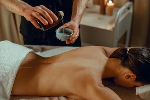 Masseur man therapist pouring warm herb infused oil to make back massage Stock Photos