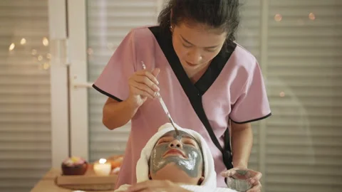 Masseuse at the spa uses a brush to apply a mud mask to a beautiful Asian woman Stock Footage 144547103