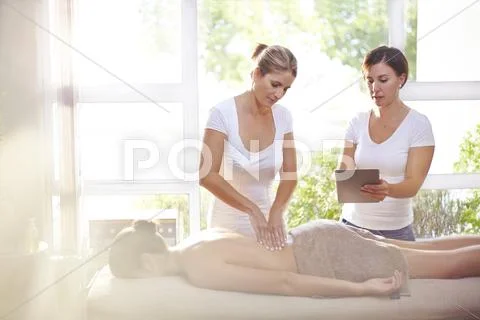 Masseuses With Digital Tablet Massaging Woman's Back