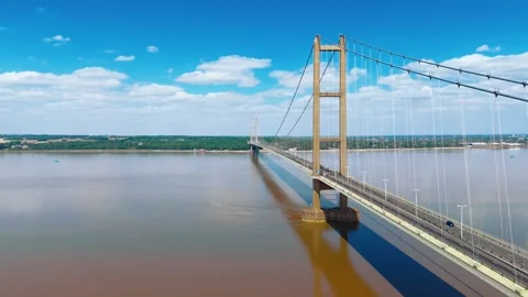 Massive bridge spans wide, muddy river under clear blue sky 스톡 동영상 343520557