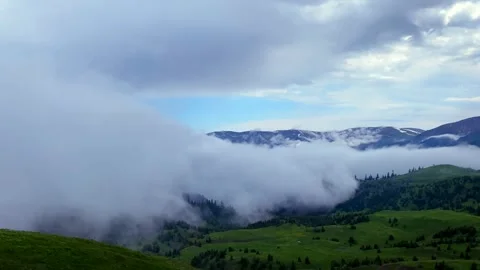 Massive cloud bank spills across a mountain ridge above alpine meadows Stock Footage 338004807