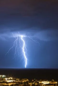 Massive cloud to ground lightning bolts hitting the horizon of city lights Stock Photos