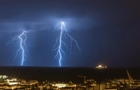 Massive cloud to ground lightning bolts hitting the horizon of city lights Stock Photos