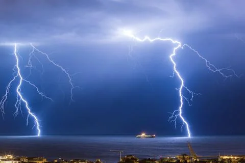 Massive cloud to ground lightning bolts hitting the horizon of city lights Stock Photos