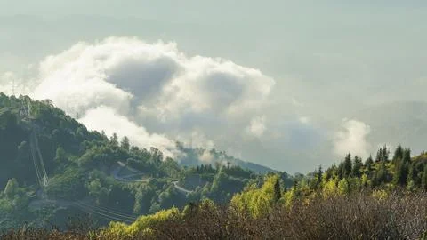 Massive clouds envelop the mountain ridge above a scenic winding road at noon Stock Photos